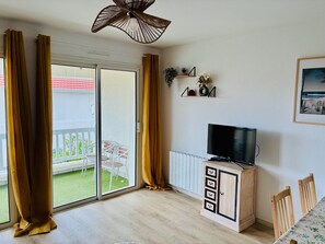 A room with a sliding glass door to a balcony, a television on a wooden cabinet, and a framed picture on the wall. - Bright apartment 160m from the beach - 6 guests (Biscarrosse Plage)