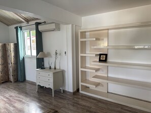 A room with a wooden floor, a white dresser, a wall-mounted air conditioner, a window with curtains, and a built-in shelving unit. - Spacious apartment - 6 guests. South Reunion (Le Tampon)