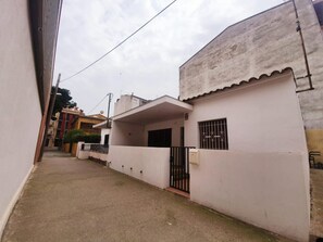 Un estrecho callejón con un edificio blanco, una entrada con reja y una antena parabólica visible.