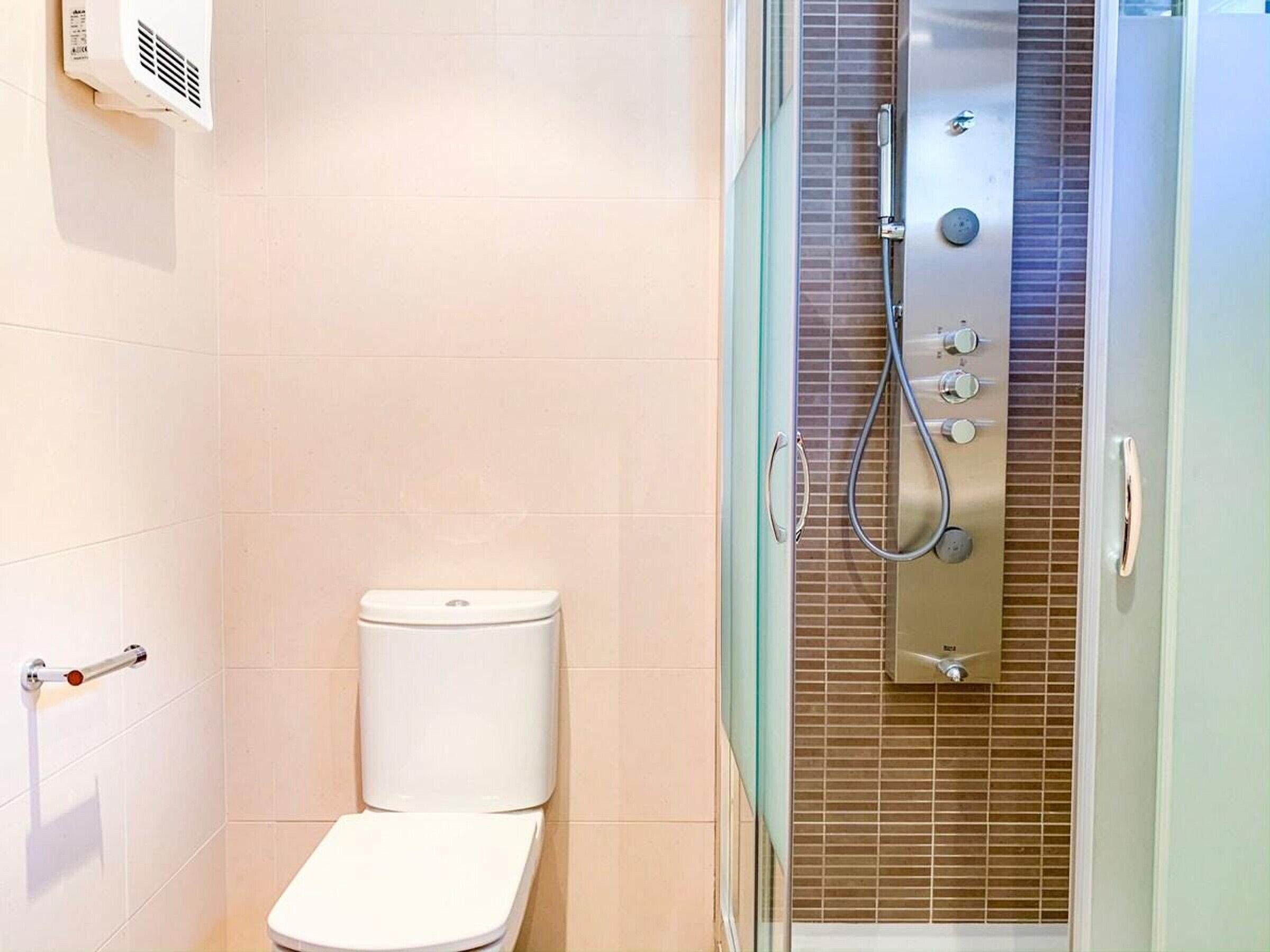 Une salle de bain comprenant des toilettes, une douche dotée d’un panneau de commande et un espace douche délimité par des parois en verre.