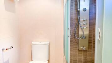 Un baño con inodoro, ducha con panel de control y zona de ducha con mampara de vidrio.