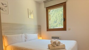 A neatly made bed with white linens, a wooden headboard, and a window with a forest view. - Modern Apartment in Arinsal - 5 pers, PARKING (Arinsal)