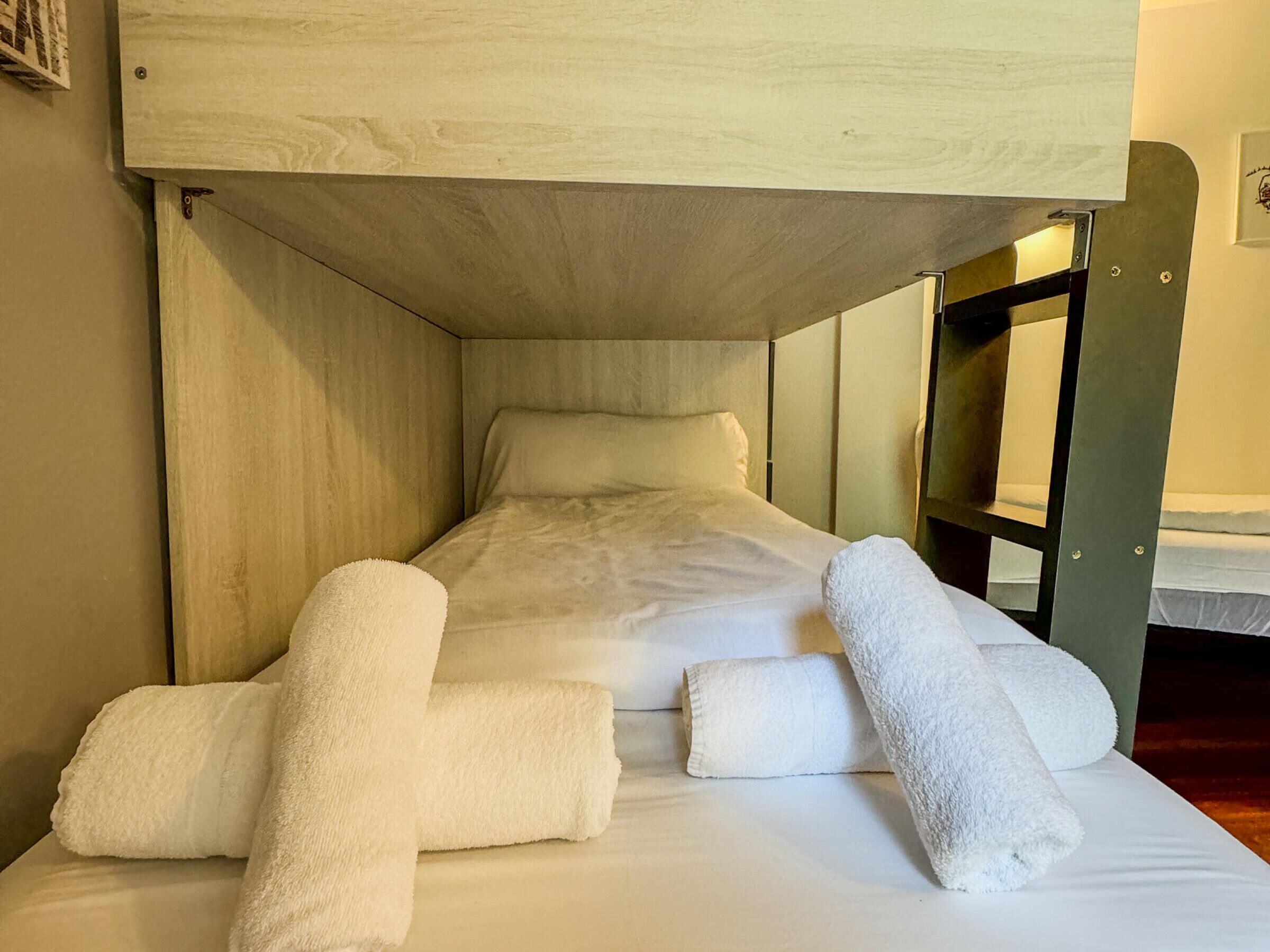 Una cama litera con cabecera de madera, un colchón blanco y dos toallas enrolladas sobre la cama.