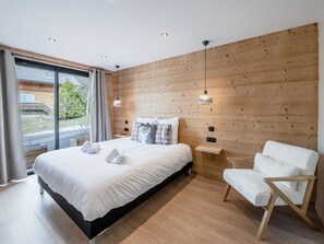 Een moderne slaapkamer met een groot bed, een houten wand, een raam met uitzicht en een witte stoel.