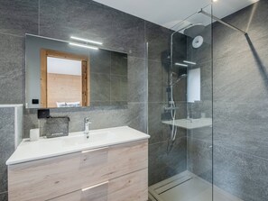 Een moderne badkamer met een douchecabine van glas, een houten wastafelmeubel met een witte wasbak en een grote spiegel erboven.