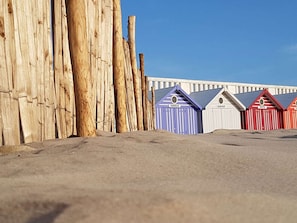 A row of beach huts with names like Vannead and Manchester, set against a backdrop of wooden poles and a clear sky. - Studio cabin, pets allowed - 5 guests, dune view (Cucq)