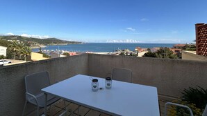 A balcony with a table and chairs, overlooking a coastal view with buildings and mountains. - Studio sea view, parking - 2 guests (Banyuls-sur-Mer)