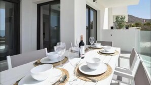 A dining table set with white plates, bowls, cutlery, and wine glasses, with a bottle of wine, on a balcony with a view of the landscape.