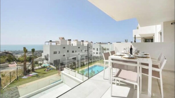 A modern apartment with a balcony overlooking a swimming pool and a cityscape.