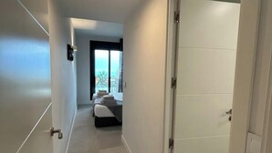 A hallway leading to a bedroom with a bed, a window, and a door.