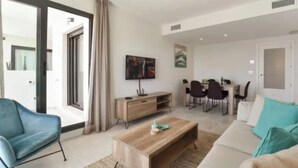 A modern living room with a sofa, coffee table, TV, and dining area.