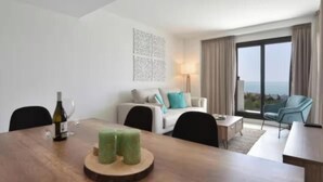 A modern hotel room with a dining table, a sofa, a chair, and a view of the outdoors.