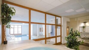 Un espace de bien-être comprenant un jacuzzi, des fenêtres à cadre en bois et des plantes d’intérieur.