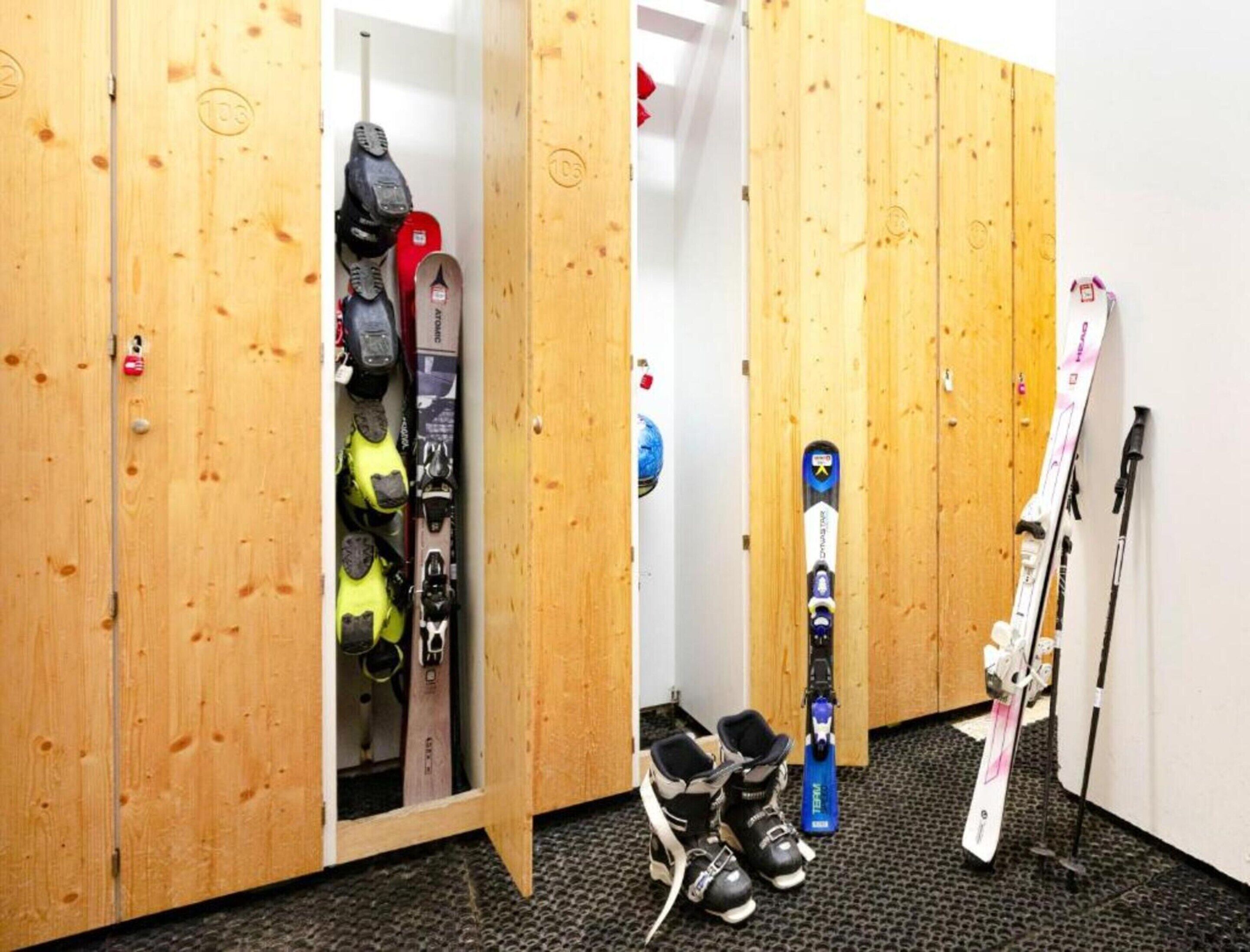Un vestuario para esquí con taquillas de madera, equipo de esquí y un par de esquíes en el suelo.