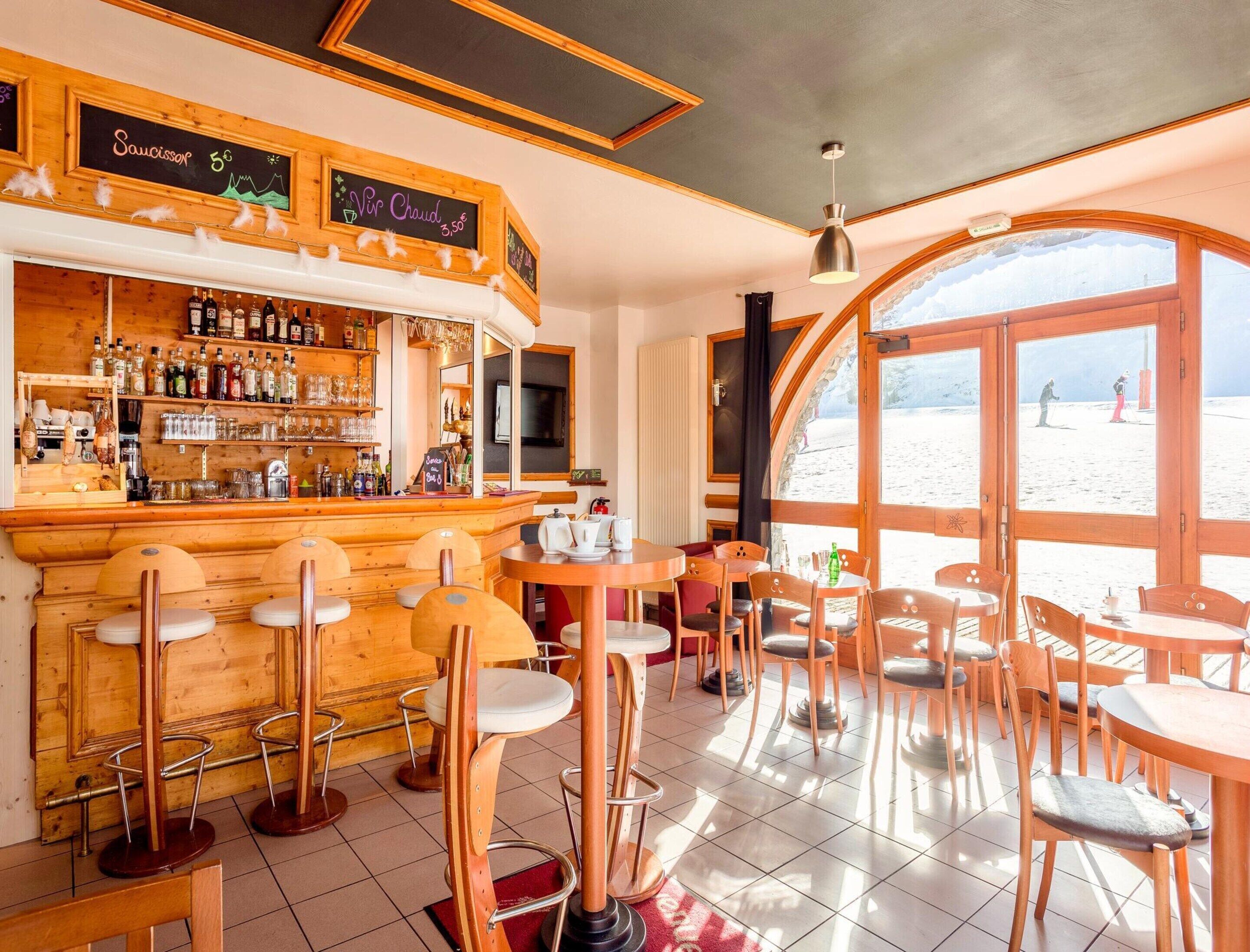 A bar area with wooden furniture, a tiled floor, and a view of the beach through large windows.