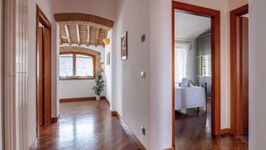 Un pasillo con piso de madera, una ventana con vistas, y una puerta que da a una habitación con cama y baño.