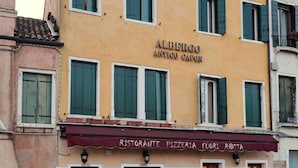 Un bâtiment sur lequel on peut lire l’inscription « ALBERGO ANTICO CAPON », et qui est surmonté d’un auvent bordeaux sur lequel est écrit « RISTORANTE PIZZERIA FUGI ROTTA ».