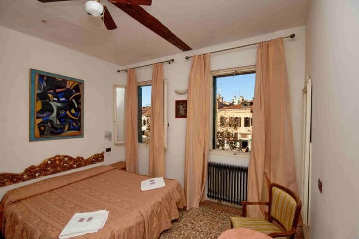 Een slaapkamer met een bed, een stoel, een radiator en een raam met gordijnen.