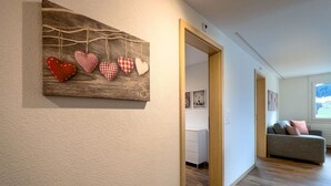 Käytävällä on puinen seinätaideteos, harmaa sohva ja ikkuna, josta on näkymä.