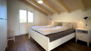 Um quarto com cama, mesas de cabeceira, um radiador e uma janela.