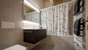 Casa de banho com sanita, lavatório com espelho em cima, suporte para toalhas e cortina de chuveiro com padrão de folhas.