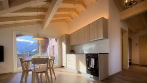 Uma cozinha moderna com armários de madeira, uma área de refeições com mesa e cadeiras, e vista para montanhas através de uma grande janela.