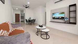 Ein modernes Wohnzimmer mit einer Couch, zwei kleinen Tischen, einem Essbereich mit Stühlen, einem Deckenventilator und einem an der Wand befestigten Fernseher.