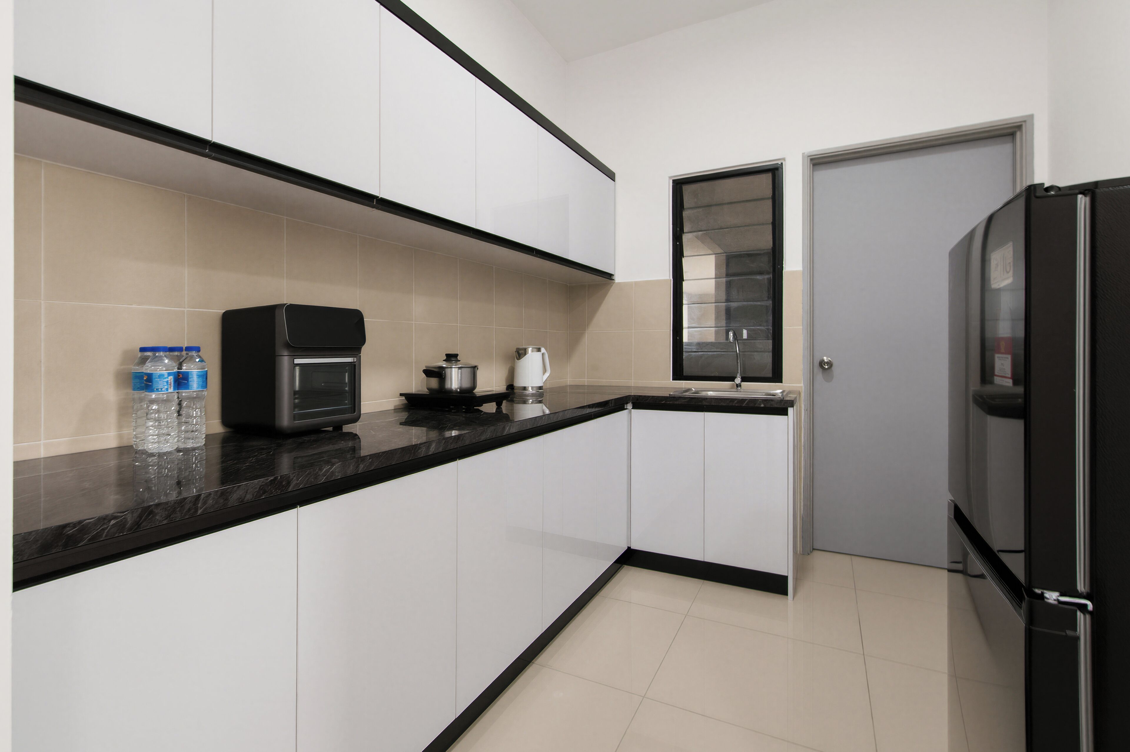 A compact kitchen with white cabinets, a black countertop, a coffee maker, a kettle, and a refrigerator.