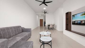 Un salon moderne avec un canapé gris, deux tables rondes, des ventilateurs de plafond, un téléviseur et un coin repas.