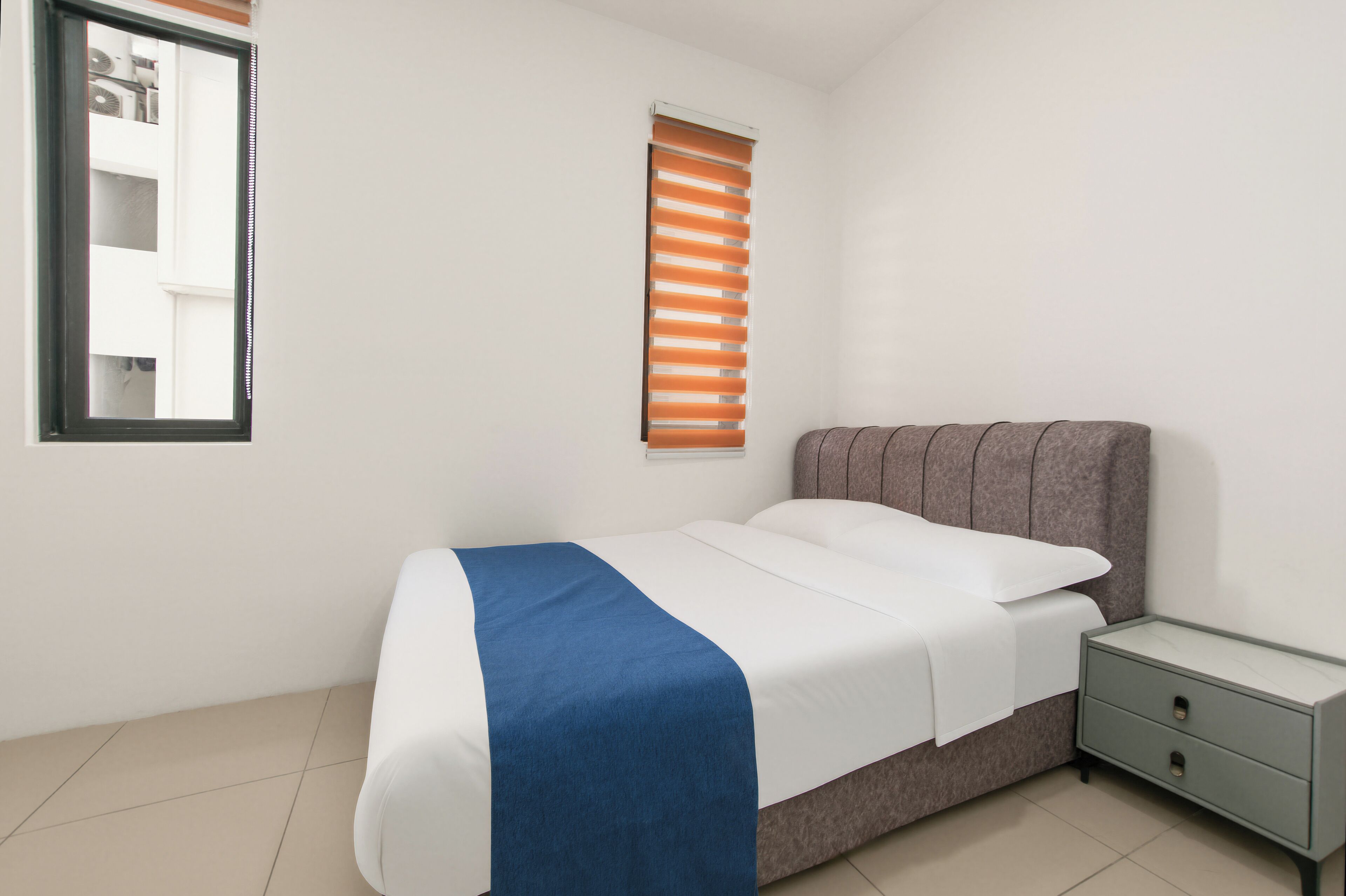 Un dormitorio con cama, mesita de noche, ventana con persianas y espejo en la pared.
