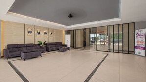 Eine moderne Lobby mit einer Couch, einem Couchtisch und einer Pflanze. An der Wand hängen gerahmte Kunstwerke und eine Glastür führt nach draußen.