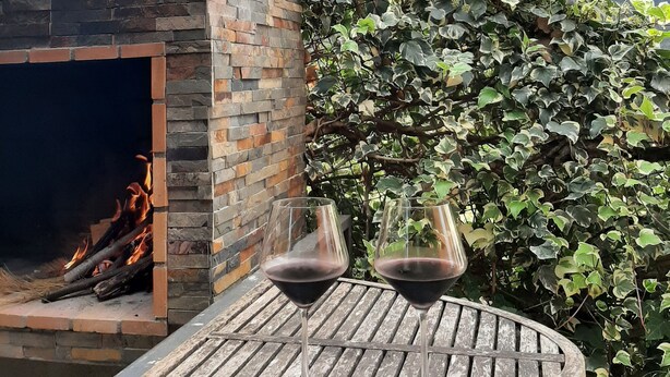 Lareira de pedra com chaminé, dois copos de vinho sobre uma mesa de madeira e vista para uma paisagem montanhosa.