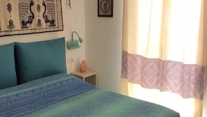 Un lit avec une couvre-lit à motifs, une table de chevet avec une lampe, une tapisserie murale et une fenêtre avec des rideaux.