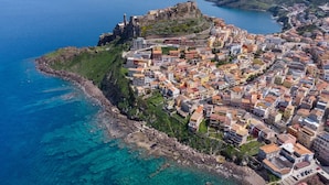 Vue aérienne d’une ville côtière, avec un fort historique, des habitations densément regroupées et des eaux d’un bleu limpide.