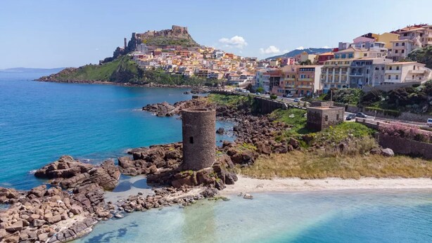 Une ville côtière qui abrite un château imposant perché sur une colline, une tour et des bâtiments aux couleurs vives le long de la côte.