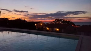 Une piscine avec vue sur un coucher de soleil et une colline parsemée de bâtiments.