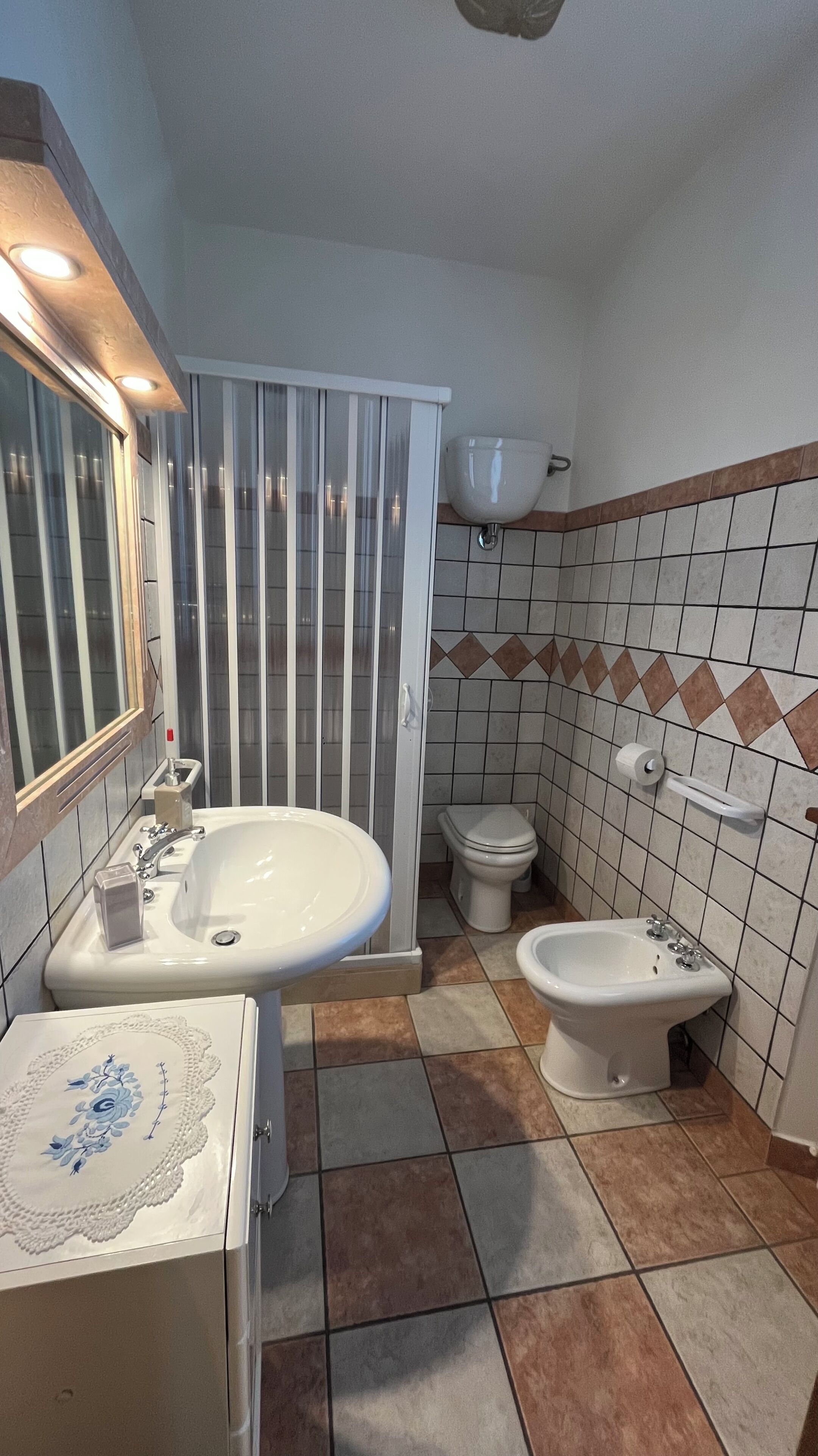 A bathroom with a sink, two toilets, a bidet, and a shower enclosure.