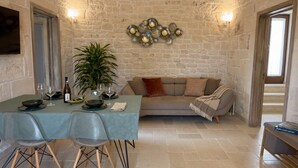 Une pièce aux murs de pierre, avec une table à manger dressée pour deux personnes, un canapé et une plante en pot.