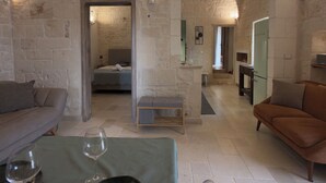 Une pièce aux murs de pierre, avec un lit, un canapé, une petite table sur laquelle se trouve un verre, et un verre à vin.
