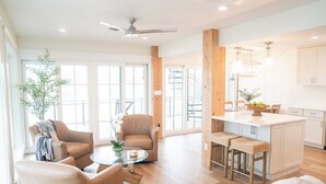 A spacious living area with a glass coffee table, two armchairs, a sofa, a kitchen island with stools, and a ceiling fan. - Bella Vista - A Quiet Lakeside Escape on 30A (Seacrest)