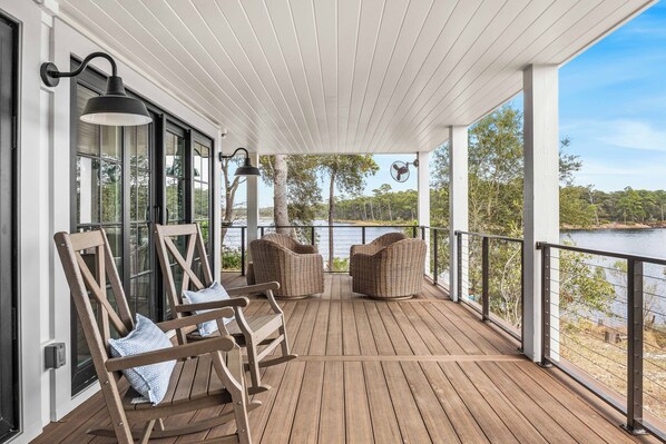 A wooden deck with wicker furniture, a railing, and a view of a lake.