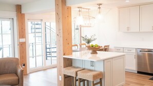 A modern kitchen with a central island, wooden beams, and a dining area with chairs. - Bella Vista - A Quiet Lakeside Escape on 30A (Seacrest)