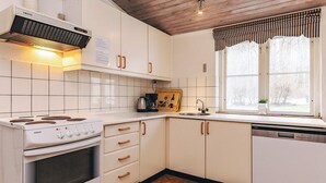 Una cocina con armarios blancos, estufa, pileta y ventana con cortinas.
