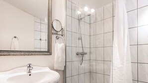 Un baño con lavamanos pedestal, un espejo, ducha con cabezal de ducha manual y piso a cuadros.