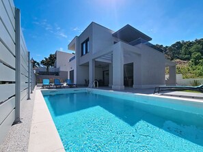 Ein modernes Gebäude mit Schwimmbad, Sitzgelegenheiten im Freien und blauem Himmel.