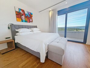 Ein modernes Schlafzimmer mit einem großen Bett, einem Nachttisch, einem Bild an der Wand und einem Balkon mit Blick.