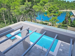 Ein Dachpool mit klarem, blauem Wasser, umgeben von Bäumen und Blick aufs Meer.