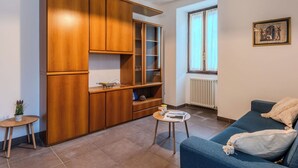 Ein Wohnzimmer mit einem blauen Sofa, einem Holzkabinett und einem kleinen Tisch mit einer Lampe.