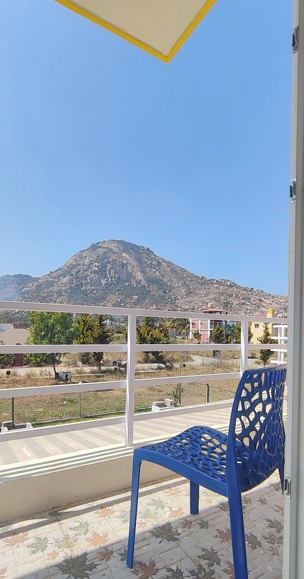Un balcon avec une chaise en plastique bleue, une vue sur une montagne et un ciel dégagé.