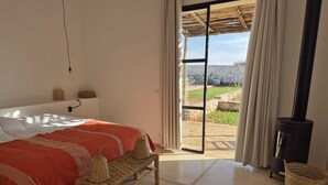 Ein Schlafzimmer mit Bett, einer Bank, einem Kamin und Blick ins Freie.
